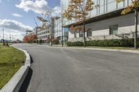 a paved road next to some buildings on a sunny day with trees in the foreground