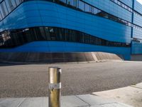 an empty street has a light pole on the side of it and a building with a curved blue exterior