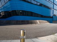 an empty street has a light pole on the side of it and a building with a curved blue exterior