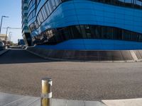 an empty street has a light pole on the side of it and a building with a curved blue exterior