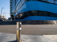 an empty street has a light pole on the side of it and a building with a curved blue exterior