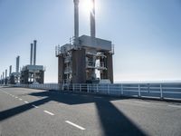 a bridge over the ocean with construction equipment in the background and two people walking on it