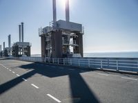 a bridge over the ocean with construction equipment in the background and two people walking on it