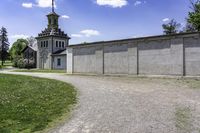 a building with a clock tower next to a dirt road and grass area outside the structure