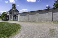 a building with a clock tower next to a dirt road and grass area outside the structure