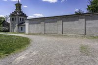 a building with a clock tower next to a dirt road and grass area outside the structure