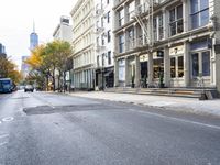 an empty street in a big city with many buildings around it and parked cars on either side