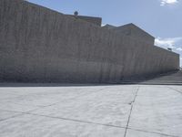 a large cement wall in an empty lot with stairs and buildings around it in the back