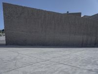 a large cement wall in an empty lot with stairs and buildings around it in the back