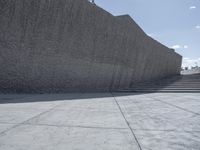 a large cement wall in an empty lot with stairs and buildings around it in the back