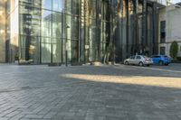 a sidewalk with cars parked on it and tall buildings reflecting in the windows of it