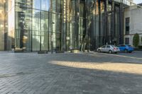 a sidewalk with cars parked on it and tall buildings reflecting in the windows of it