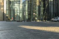 a sidewalk with cars parked on it and tall buildings reflecting in the windows of it