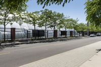 a paved side walk between two trees, a sidewalk and a metal fence along a road