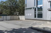 the back side of an apartment building with a fenced off entrance is a white car parked near it