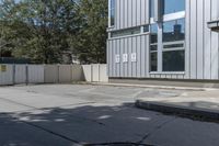 the back side of an apartment building with a fenced off entrance is a white car parked near it