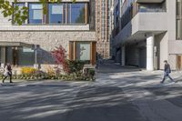 people walk around an empty courtyard surrounded by large buildings on both sides of a street