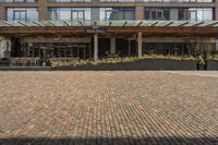 large brick sidewalk in front of building, with green roof and covered restaurant area on the ground