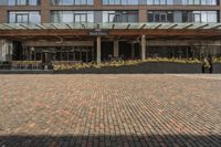 large brick sidewalk in front of building, with green roof and covered restaurant area on the ground