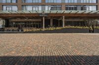 large brick sidewalk in front of building, with green roof and covered restaurant area on the ground