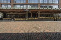 large brick sidewalk in front of building, with green roof and covered restaurant area on the ground