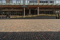 large brick sidewalk in front of building, with green roof and covered restaurant area on the ground