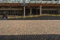 large brick sidewalk in front of building, with green roof and covered restaurant area on the ground