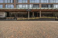 large brick sidewalk in front of building, with green roof and covered restaurant area on the ground