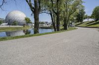 the paved road is near a small pond and dome shaped structure with a domed roof