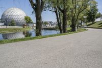 the paved road is near a small pond and dome shaped structure with a domed roof