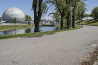 the paved road is near a small pond and dome shaped structure with a domed roof