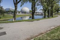 the paved road is near a small pond and dome shaped structure with a domed roof