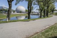 the paved road is near a small pond and dome shaped structure with a domed roof