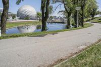 the paved road is near a small pond and dome shaped structure with a domed roof