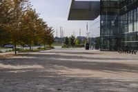 the sidewalk is made from brick and trees are in front of a glass walled building