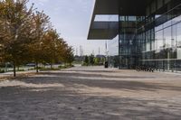 the sidewalk is made from brick and trees are in front of a glass walled building