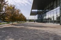 the sidewalk is made from brick and trees are in front of a glass walled building