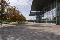 the sidewalk is made from brick and trees are in front of a glass walled building