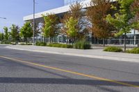 street in front of an office building with trees on both sides of the road and two cars driving down the road