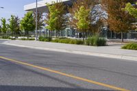 street in front of an office building with trees on both sides of the road and two cars driving down the road