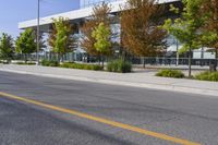 street in front of an office building with trees on both sides of the road and two cars driving down the road