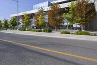 street in front of an office building with trees on both sides of the road and two cars driving down the road