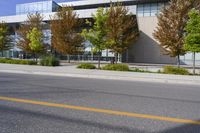 street in front of an office building with trees on both sides of the road and two cars driving down the road