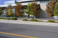 street in front of an office building with trees on both sides of the road and two cars driving down the road