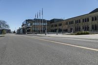 an empty street next to a tall brown building with flags on the sides of it