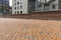 red brick floor with two building in the background from top of a roof and on the ground is a brick wall