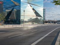 a sign stands on the corner of a paved street in front of a building with a triangle shaped glass structure