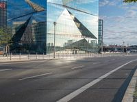 a sign stands on the corner of a paved street in front of a building with a triangle shaped glass structure