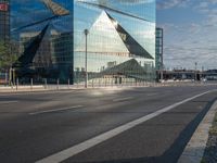 a sign stands on the corner of a paved street in front of a building with a triangle shaped glass structure