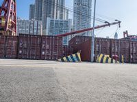 a crane near a long metal fence on top of a road with shipping boxes in the background